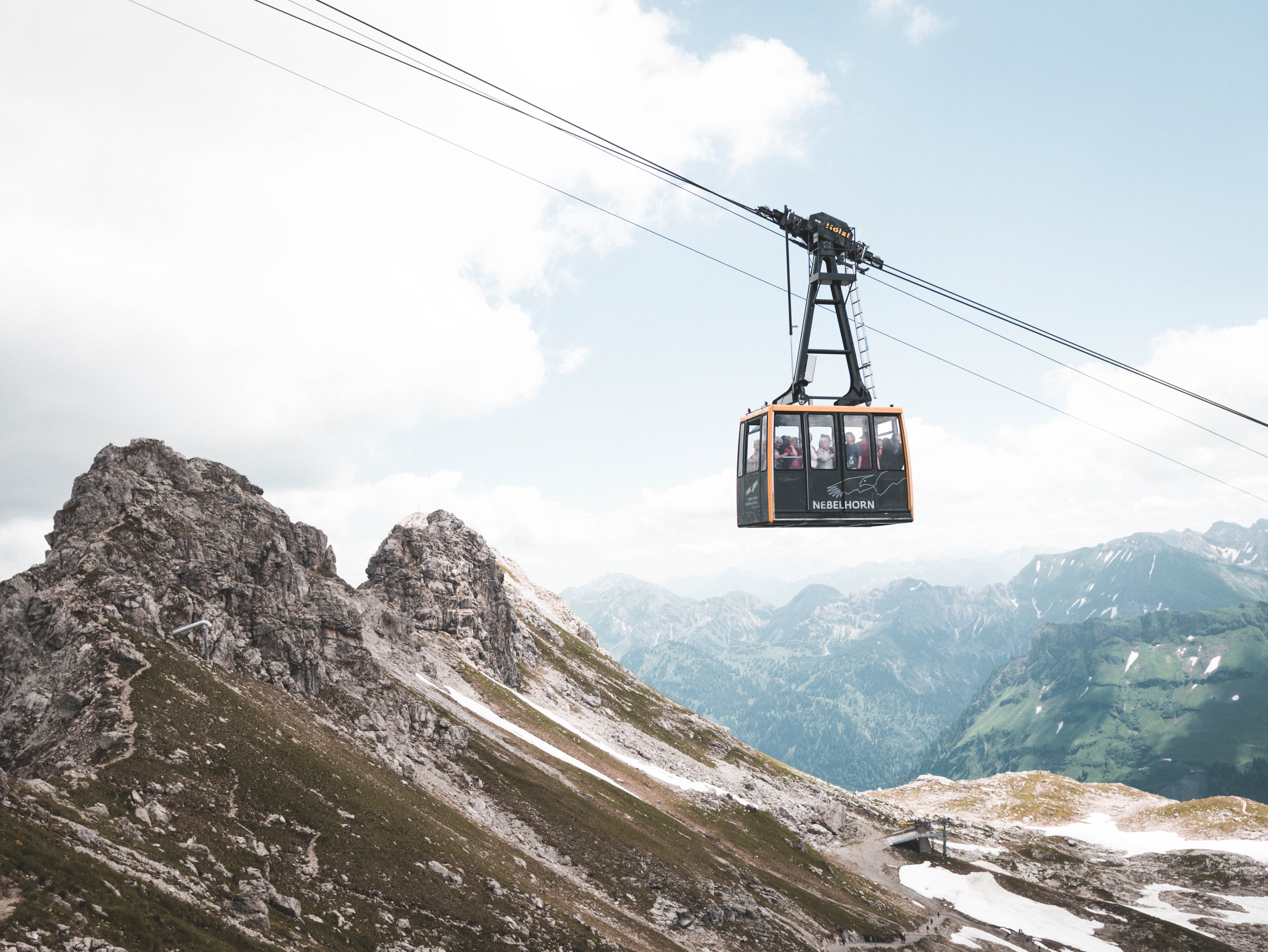 A black and orange cable cart moving people above mountains