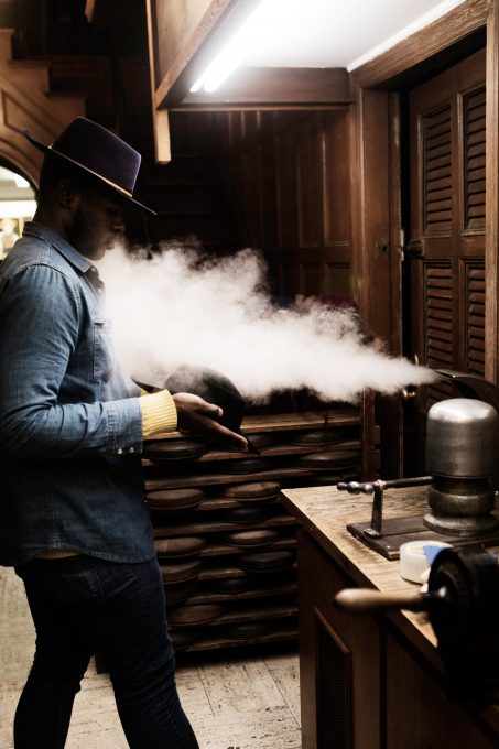 A hat maker wearing a hat standing with steam blowing out