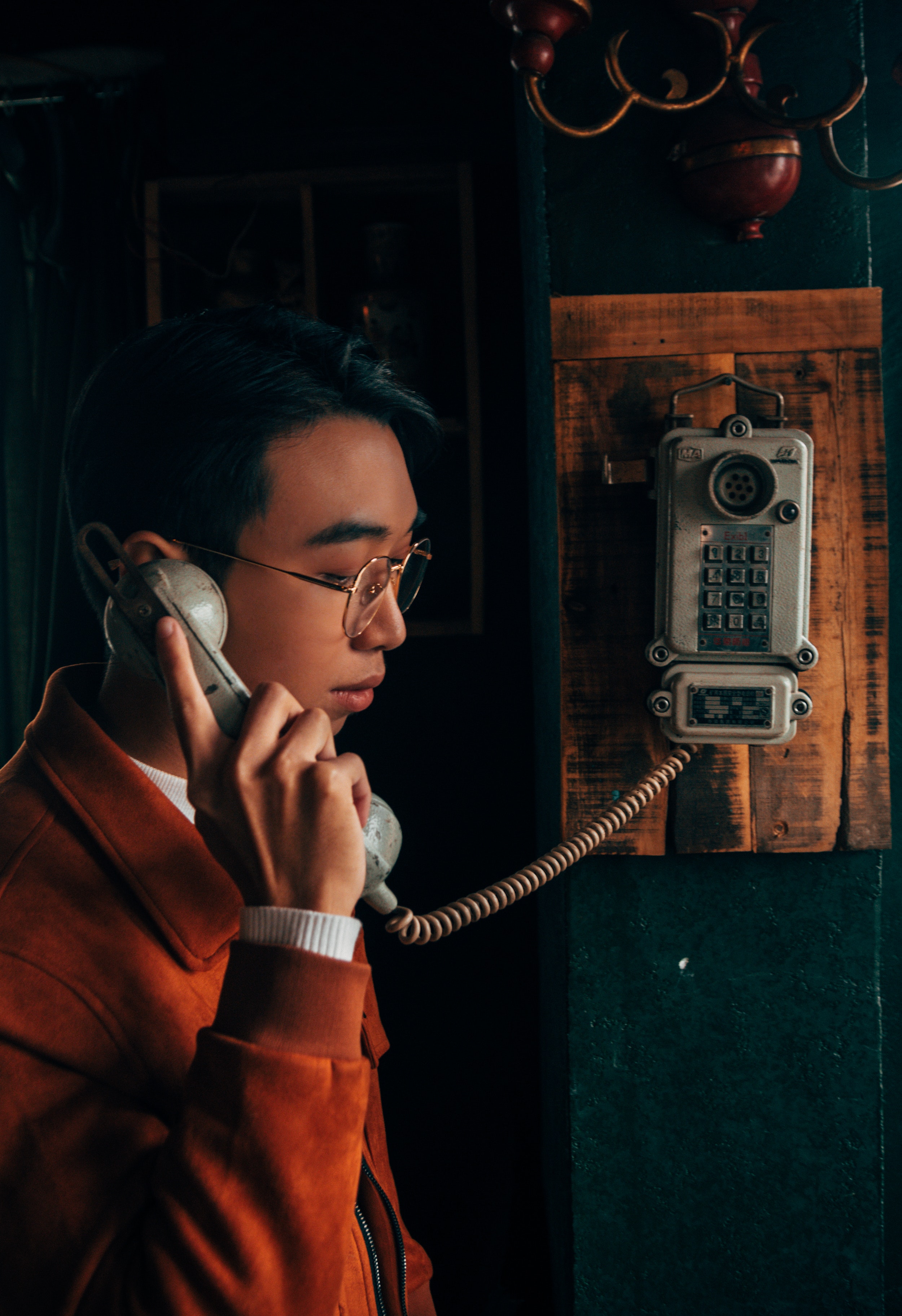 A man wearing a red jacket and glasses holding a gray cradle telephone