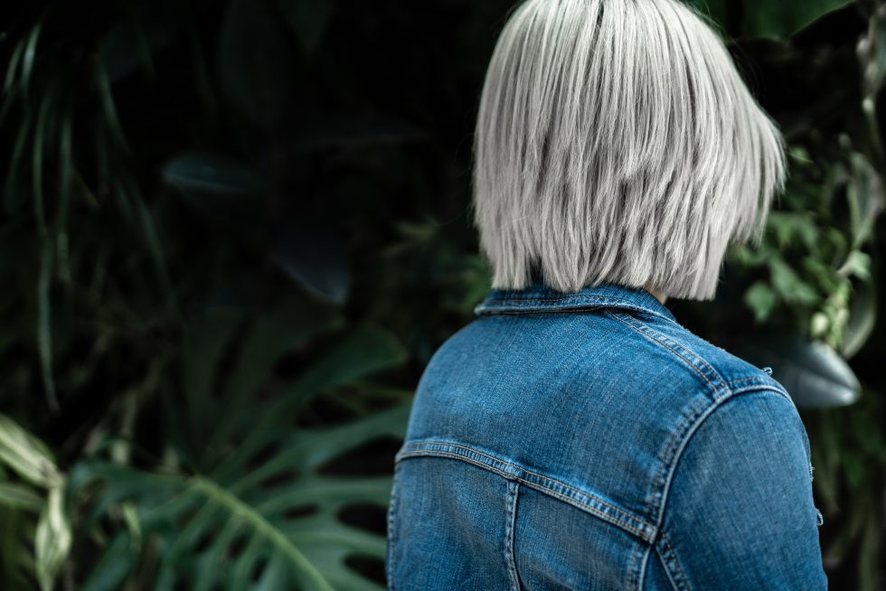 a-person-wearing-a-blue-denim-jacket-on-the-background-of-lush-greenery