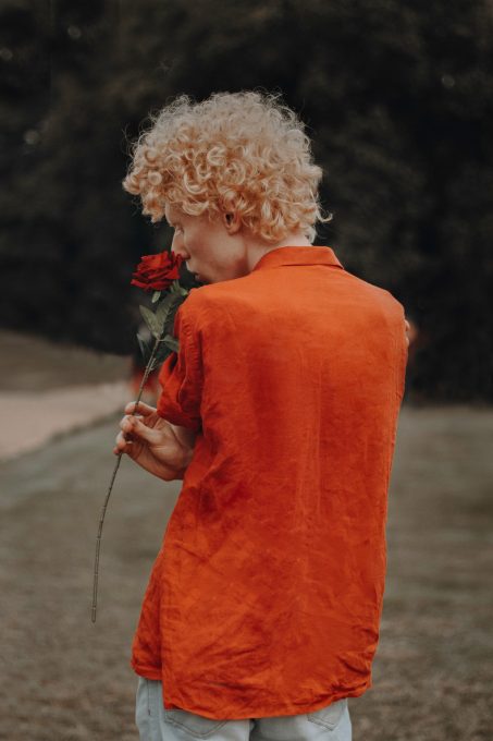 A person wearing orange dress shirt holding a red rose