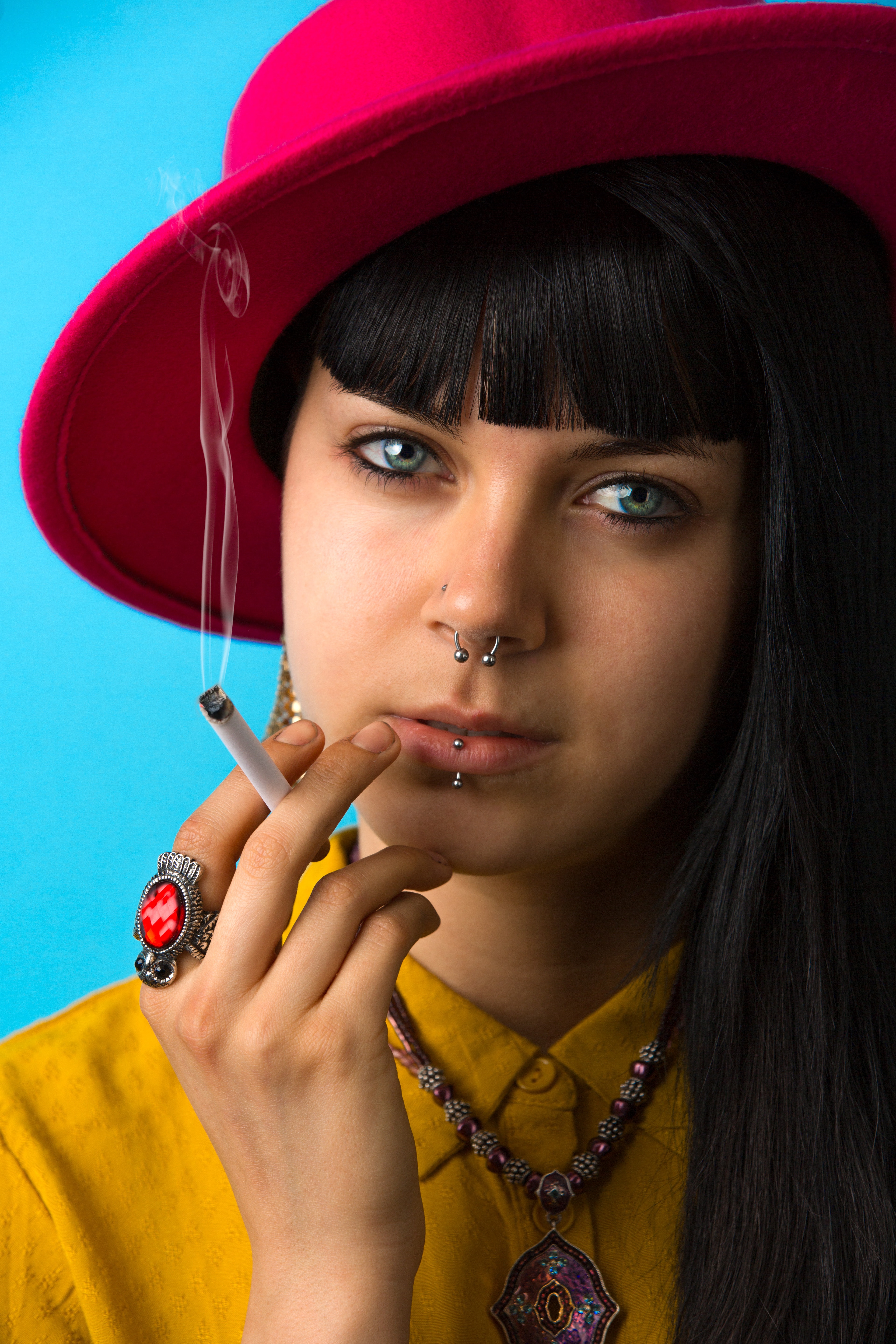 A woman holding a cigarette stick wearing a red hat and a yellow shirt