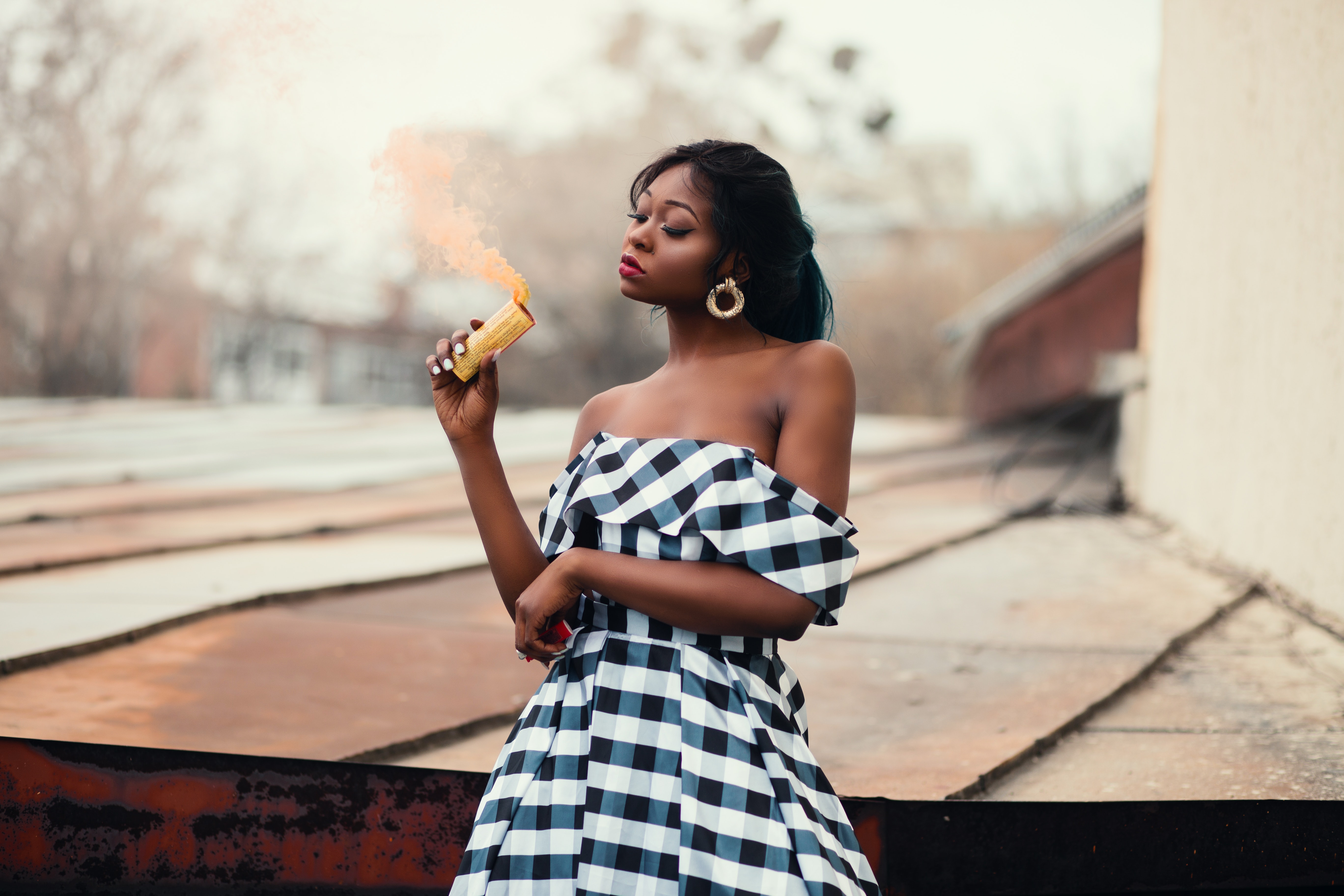 A woman in a black and white off-shoulder dress holding a smoke bomb