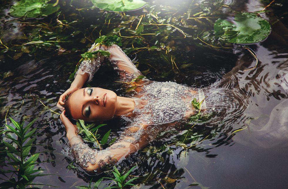 A woman in a long-sleeved dress surrounded by water plants