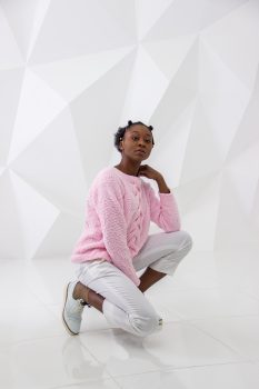 A woman wearing a pink sweater and white pants posing