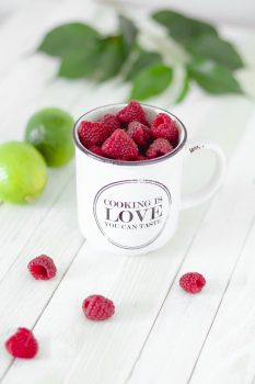 Close-up photo of an enamel cup filled with raspberries
