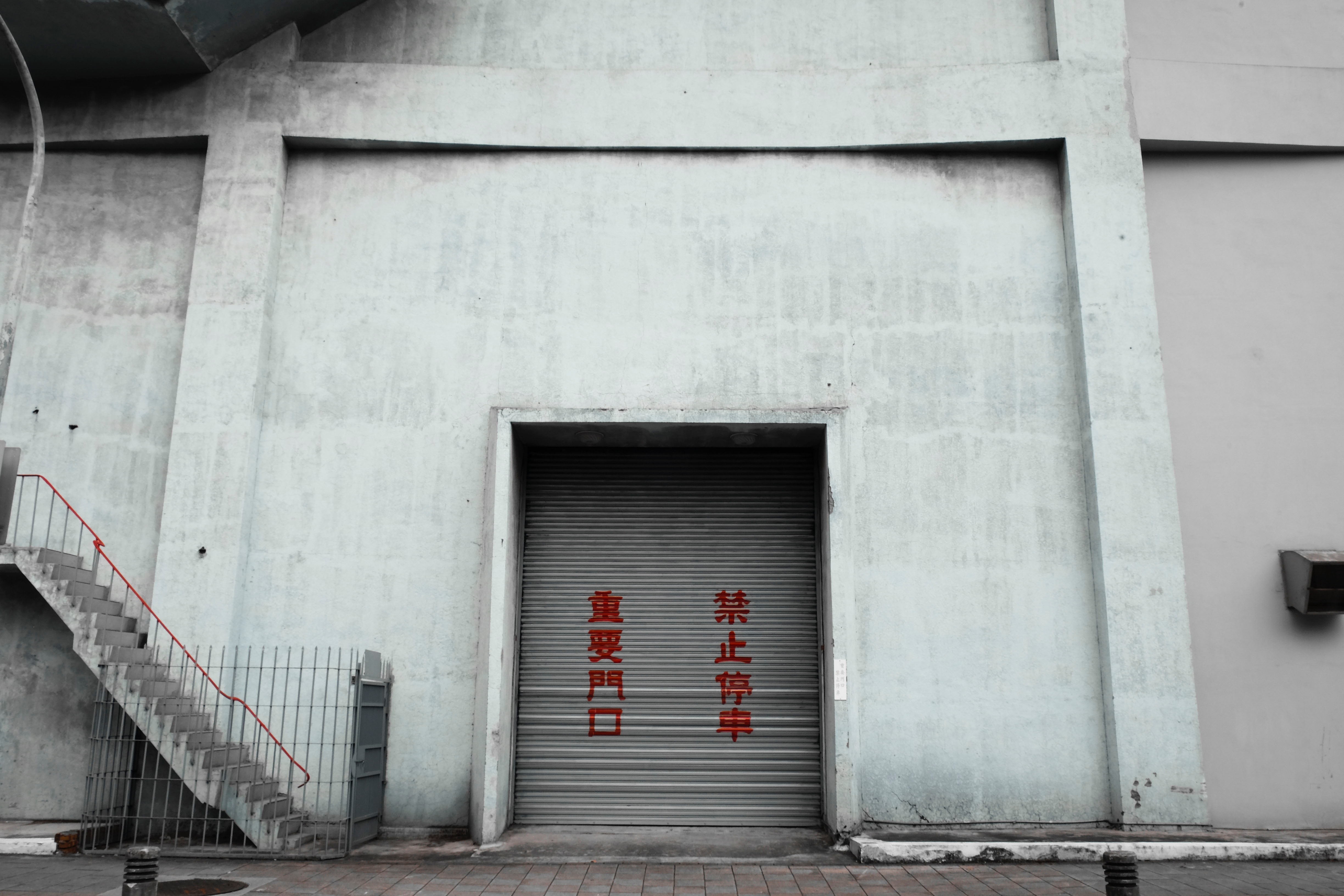 A facade of a gray building with a gate closed by roller shutter