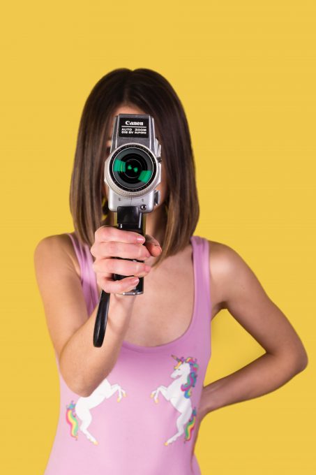 A girl wearing a pink tank top holding Canon camera