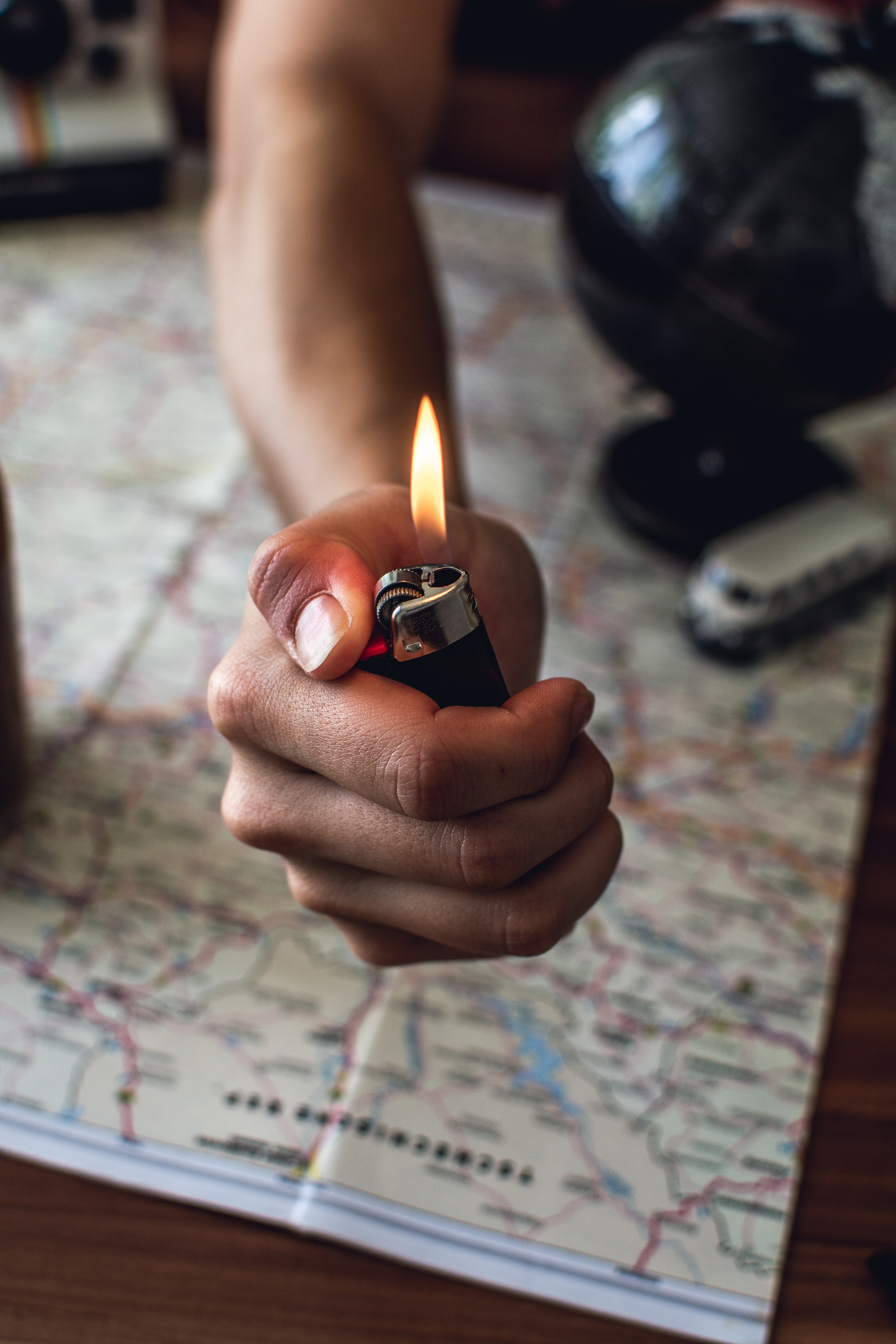 A person holding a lit lighter over a map and table globe