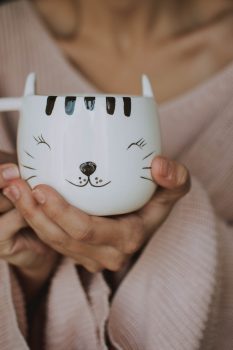 A person holding a white cat mug