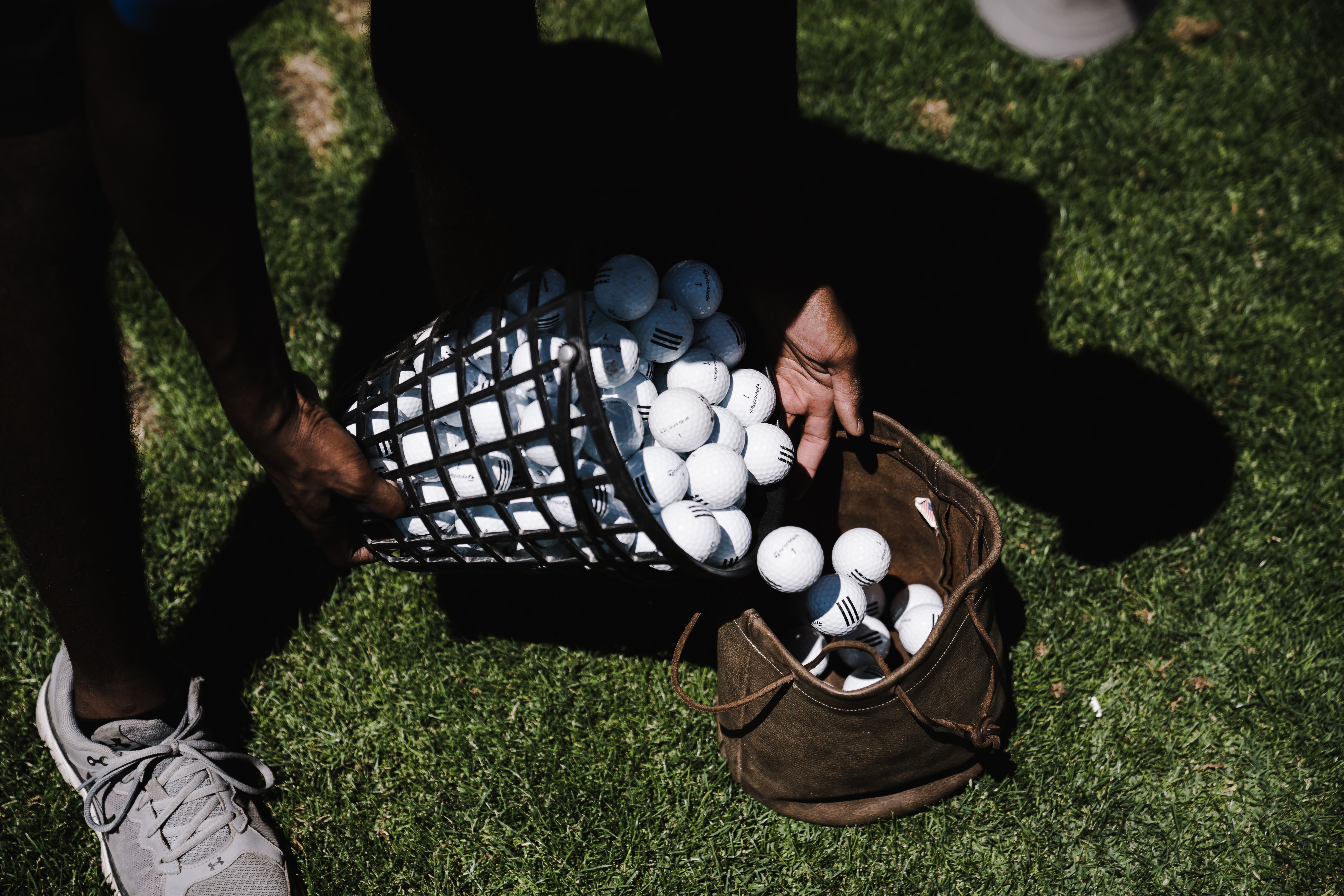 A person pouring golf balls in a brown leather bag