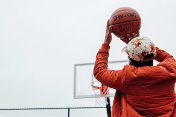 A person wearing an orange jacket and cap holding a basketball