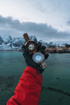 A person wearing leather gloves holding a compass in front of mountains