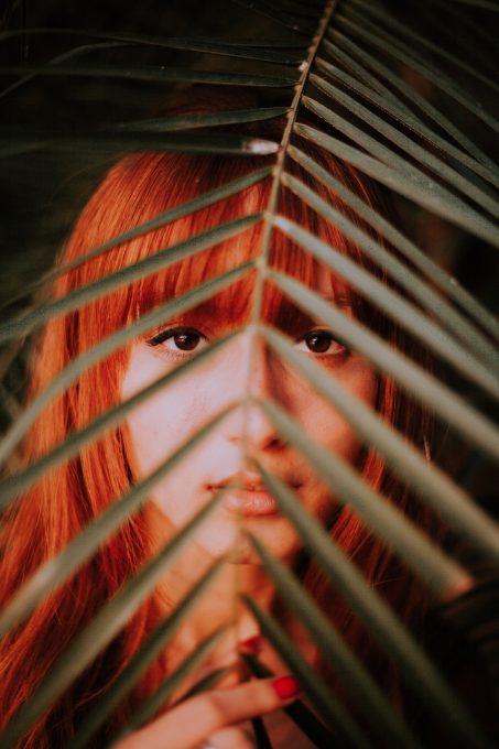 A red-haired woman behind a palm leaf