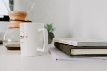 A white mug standing near books on a white table