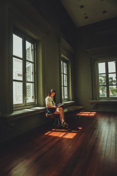 A woman sitting on a chair by a window reading a book