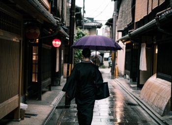 A woman using a purple umbrella walking in the street