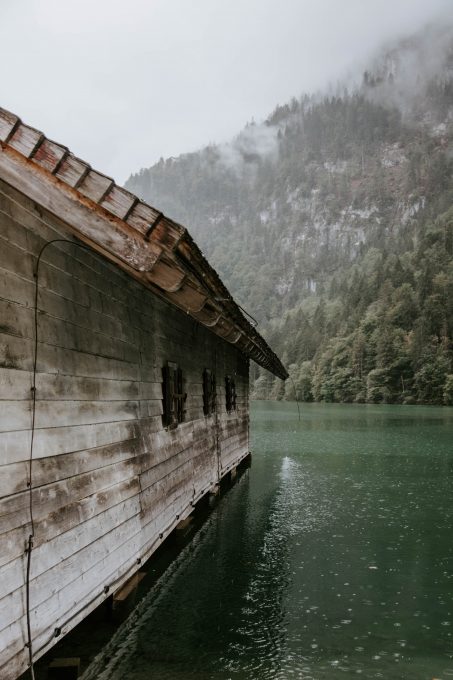 A wooden cabin surrounded by a body of water in front of foggy mountain