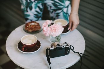 Pink flowers in a glass jar near and a cup of coffee a camera