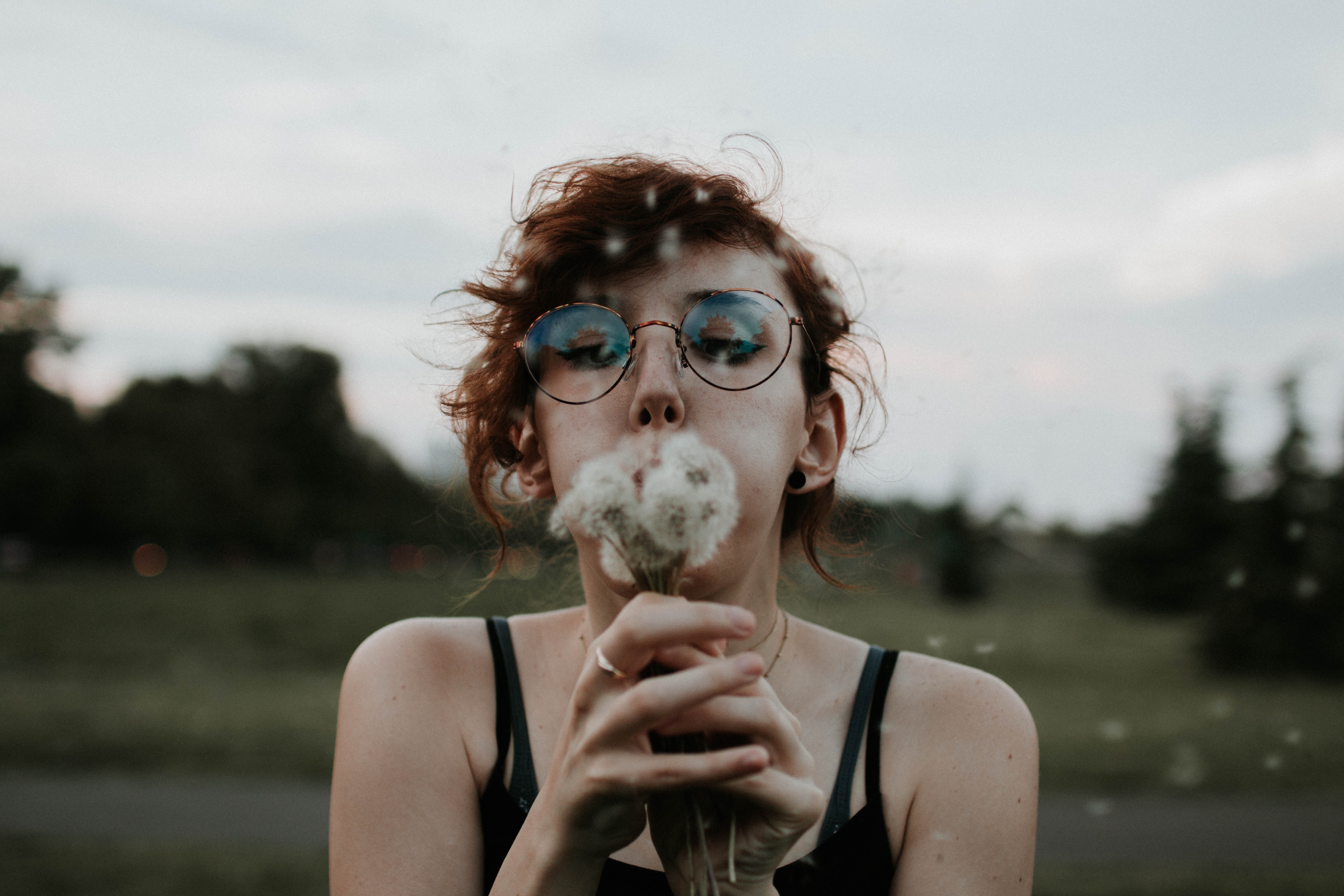 Selective focus photography of a woman blowing dandelion flowers