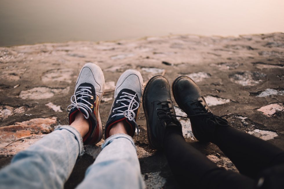 Two persons wearing pants and shoes sit on the ground at daytime