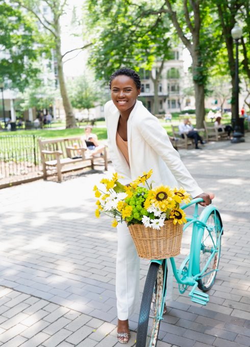 A smiling woman holding a blue cruiser bike with a basket of flowers