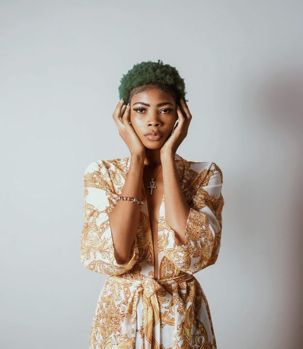 A standing woman with green hair holding both hands on her face