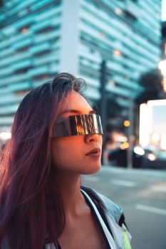 A woman wearing futuristic sunglasses near high-rise buildings