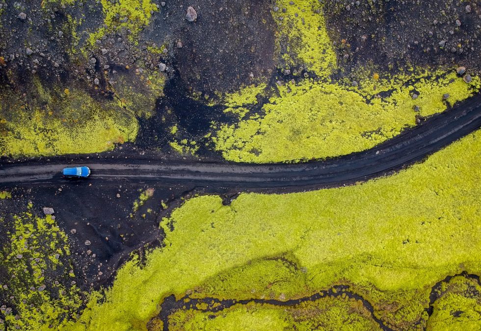 Aerial view of a car crossing over an Icelandic black lava field
