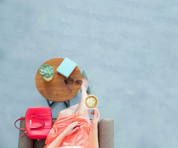 Flatlay photo of a woman sitting on a sofa chair holding a cup of coffee