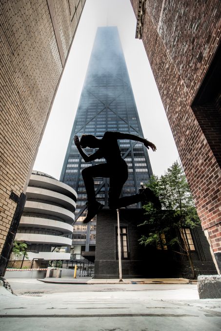 Low-angle photography of a person jumping in front of a skyscraper