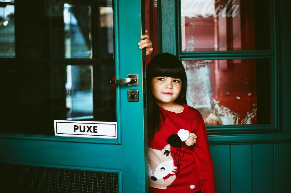 A girl wearing a red long-sleeved shirt leaning on a door