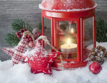A lighted white tealight candle inside a red metal lantern