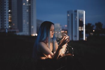 A woman holding string lights while sitting on the roof of a high building