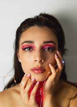 A woman wearing pink eye makeup holding string lights