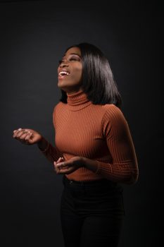Laughing woman in a brown sweater against a black wall
