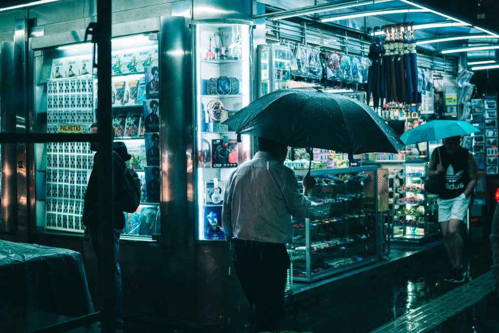 People walking along a sidewalk of a store in the evening in the rain