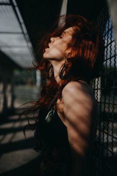 Photo of a woman leaning on a chain-link fence with her chin up