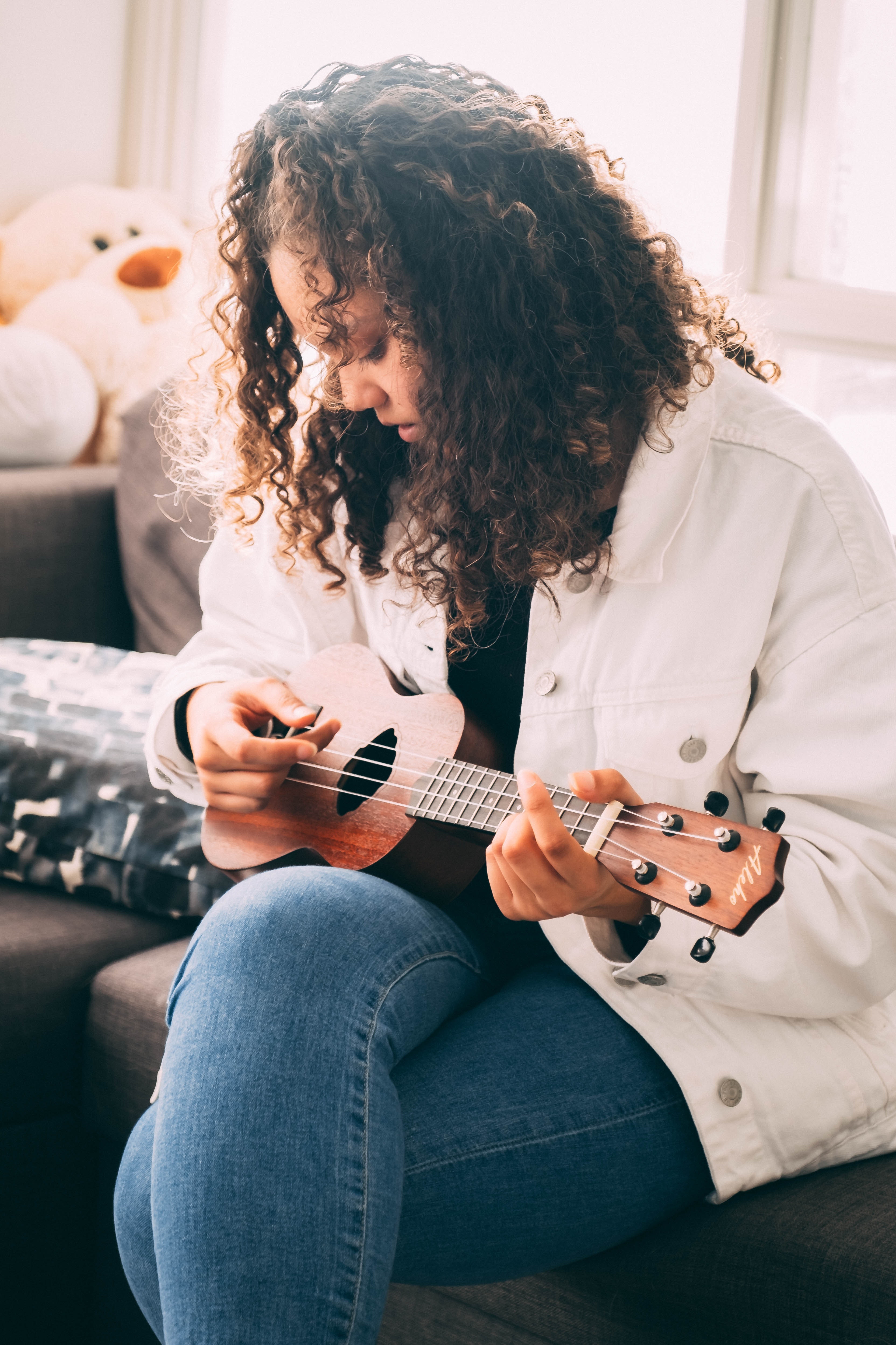 Photo of a woman playing ukulele sitting on a gray sofa