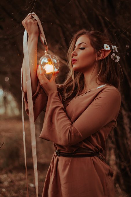 Shallow focus photo of a woman in a brown dress holding a candle