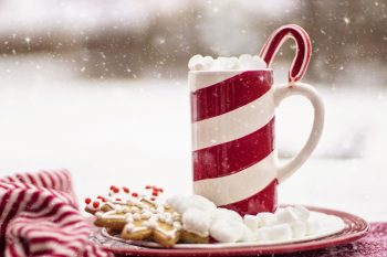 Snow falling on a mug with marshmallows and Christmas cookies on a plate