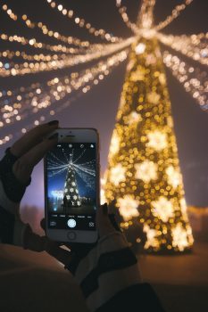 A person taking a picture of an illuminated Christmas tree