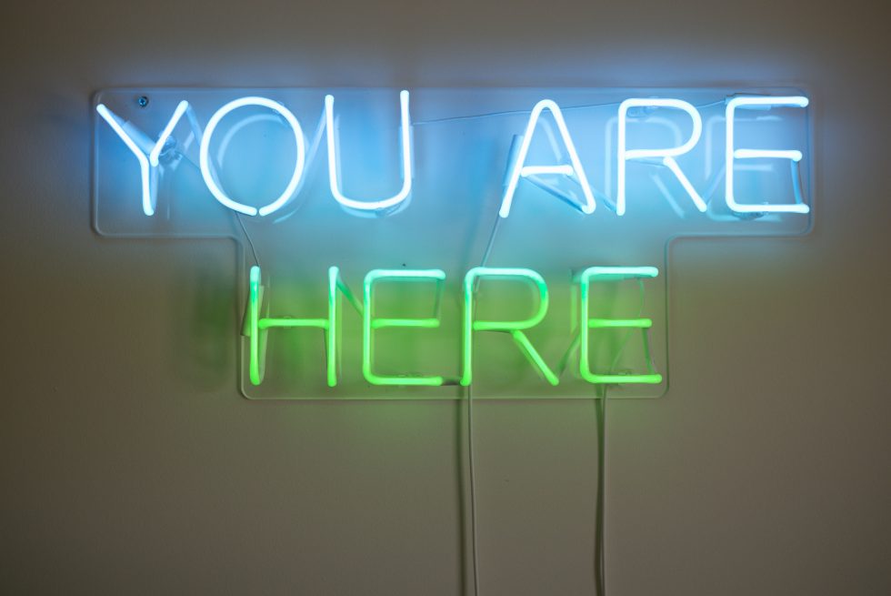 A neon blue and green sign you are here on the wall