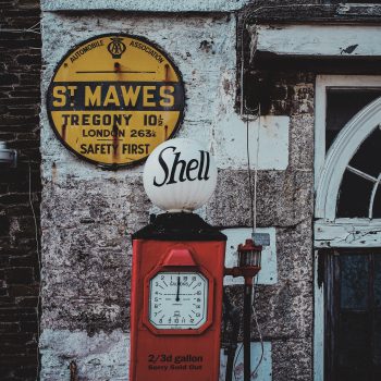 A red petrol pump by an old wall with a yellow sign