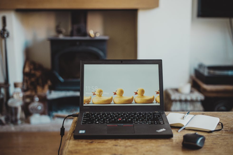 An open laptop with duck background and a notebook on a desk