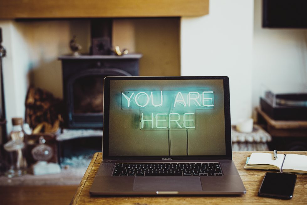 An open laptop with you are here background and notebook with cellphone on a desk